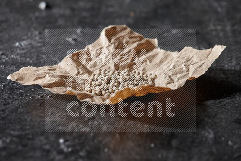 White pepper beads in a crumpled piece of on textured black flooring
