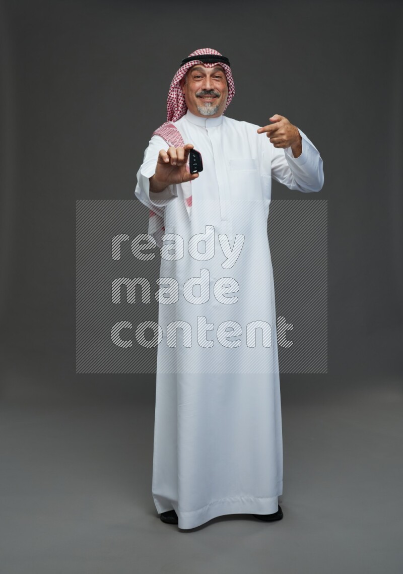 Saudi man with shomag Standing holding car key on gray background
