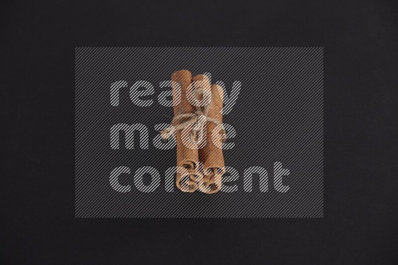 4 Cinnamon sticks stacked and bounded on black flooring