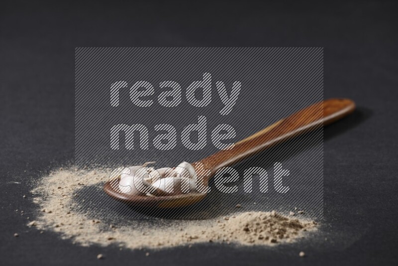 ملعقة خشبية كبيرة مليئة بفصوص الثوم مع بعض من بودرة الثوم المتناثرة على خلفية سوداء