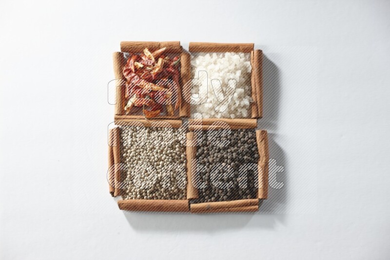 4 مربعات من أعواد القرفة ممتلئة بالفلفل الأحمر والملح والفلفل الأبيض والفلفل الأسود على أرضية بيضاء
