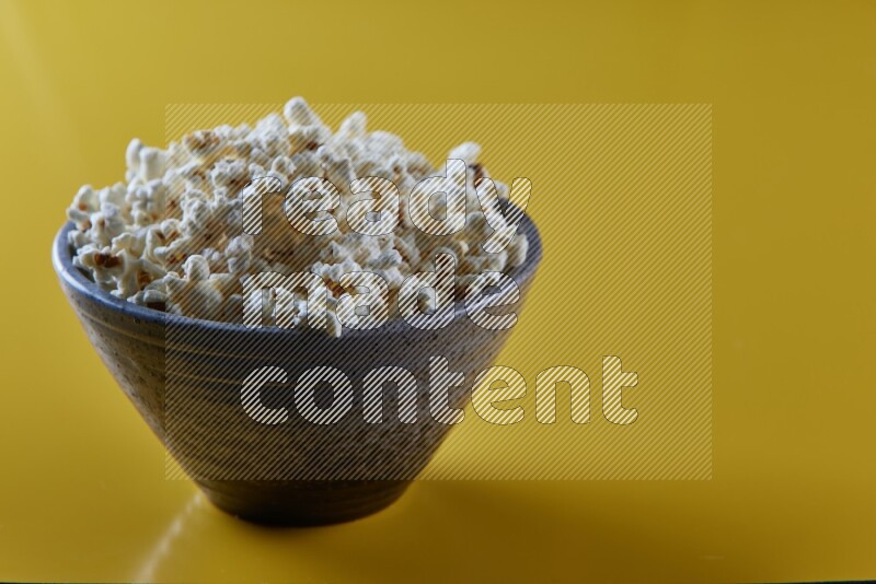 A multicolored pottery bowl full of popcorn on a yellow background in different angles