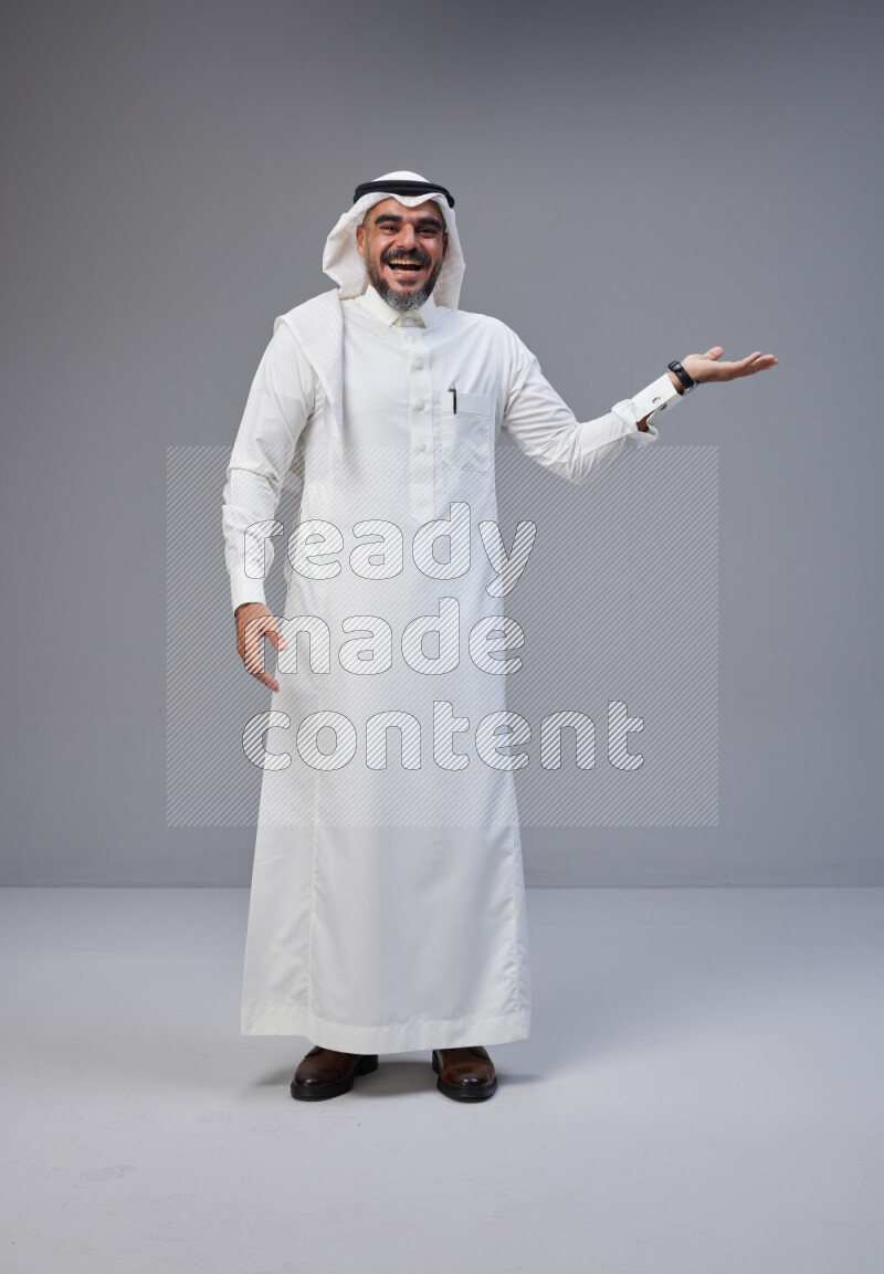 Saudi man Wearing Thob and white Shomag standing interacting with the camera on Gray background