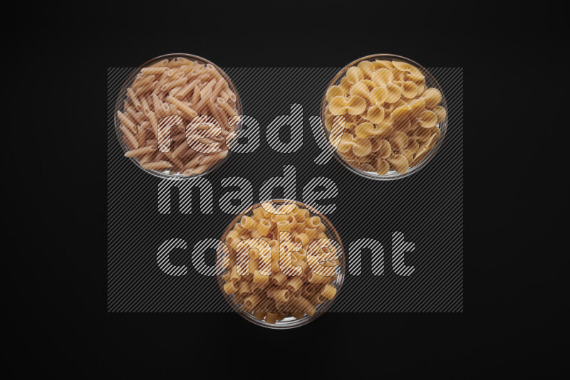Different pasta types in glass bowls on black background