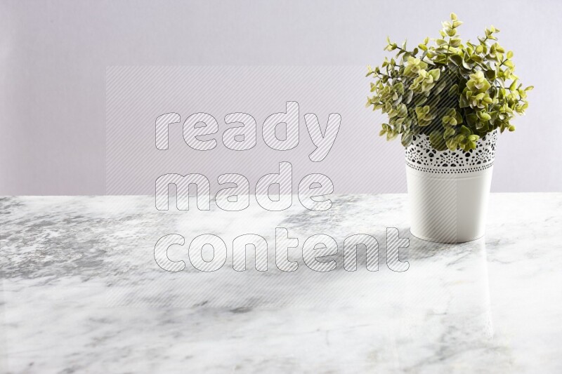 Green artificial plant in white decorative pot on grey marble background