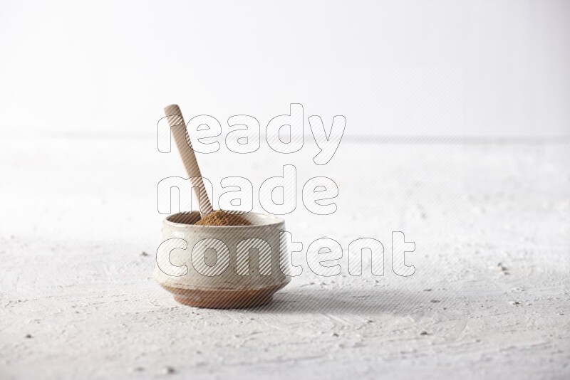 Ceramic beige bowl full of cinnamon powder with a wooden spoon on a textured white background