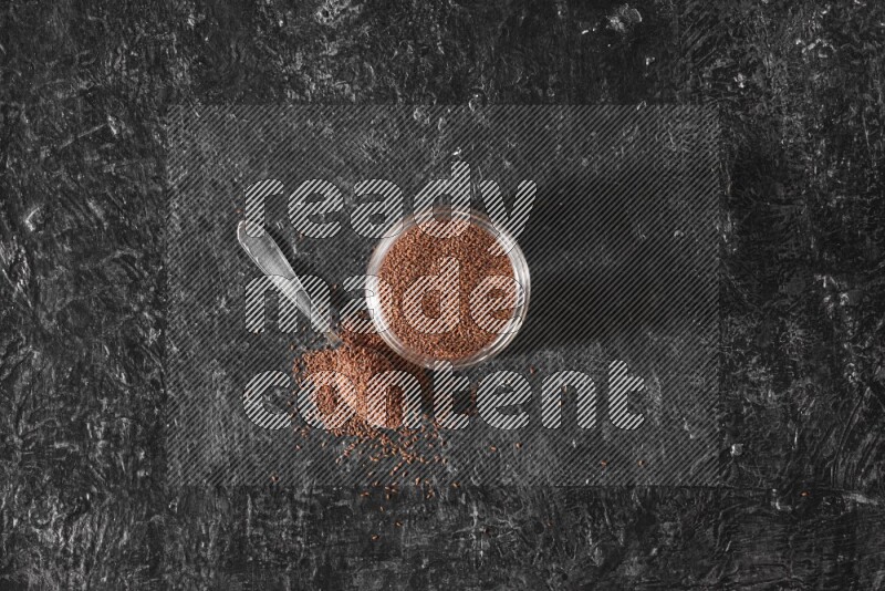 وعاء زجاجي ممتلئ ببذور حب الرشاد مع ملعقة معدنية ممتلئة بالبذور على أرضية سوداء