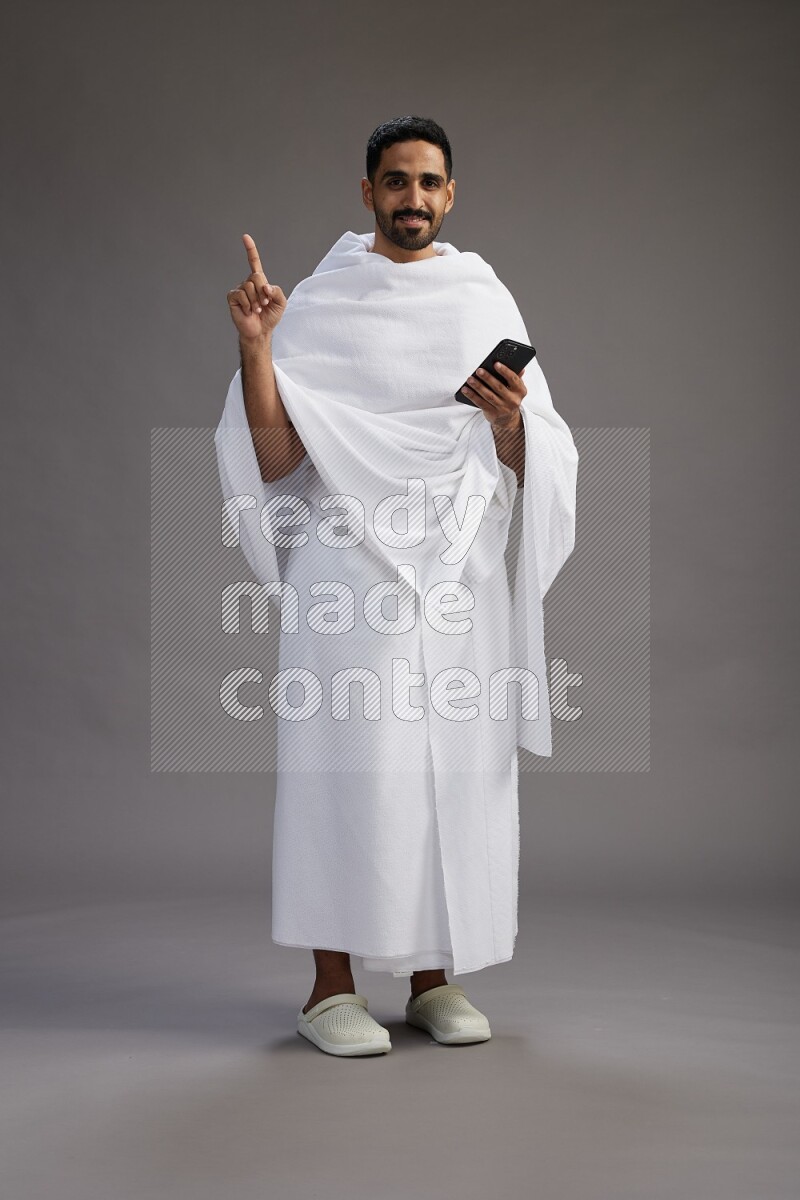 A man wearing Ehram Standing texting on phone on gray background