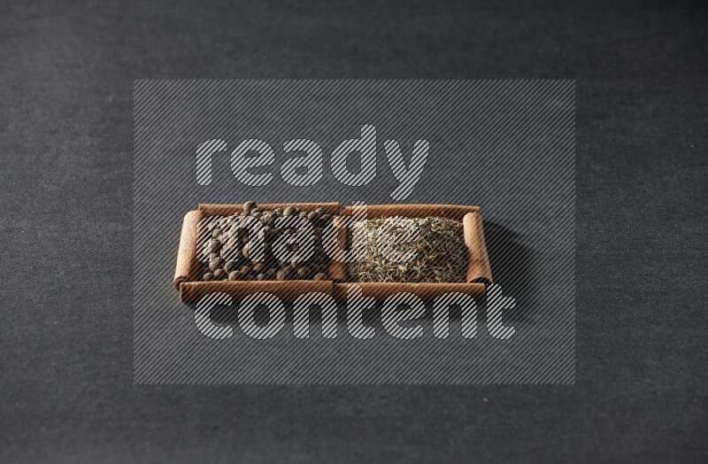 مربعان من أعواد القرفة ممتلئان بحبوب الكمون وحبوب بهار الفلفل الحلو علي خلفية سوداء