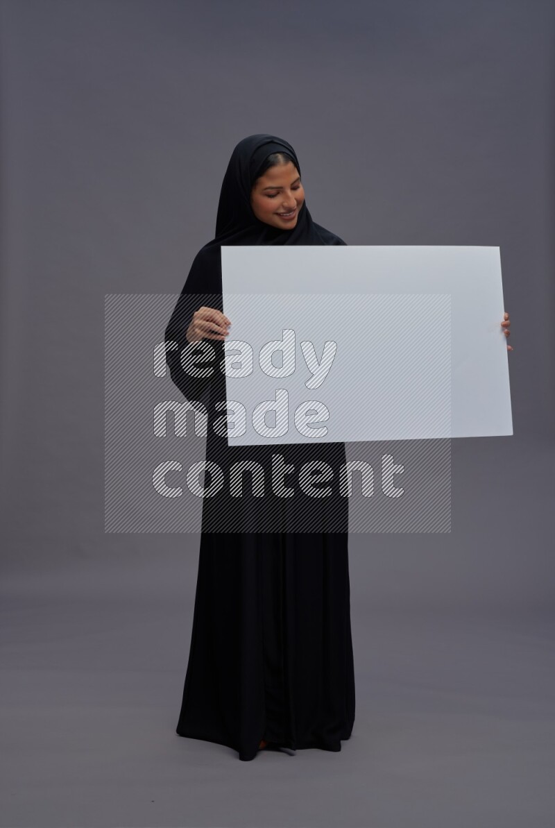 Saudi woman wearing Abaya standing holding white board on gray background
