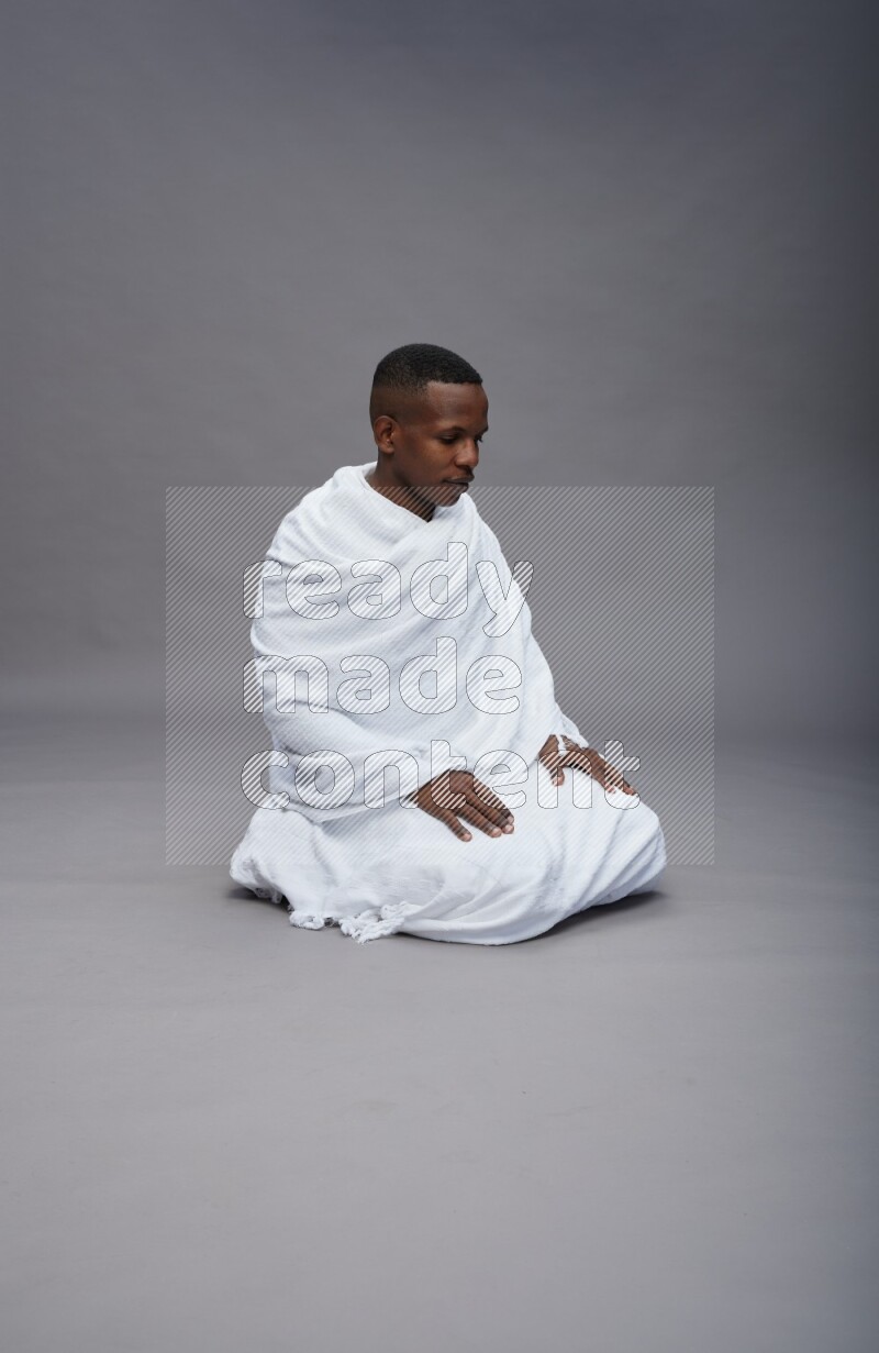 A man wearing Ehram sitting on floor praying on gray background