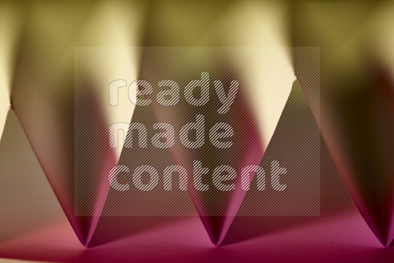 A close-up abstract image showing sharp geometric paper folds in pink gradients and warm tones