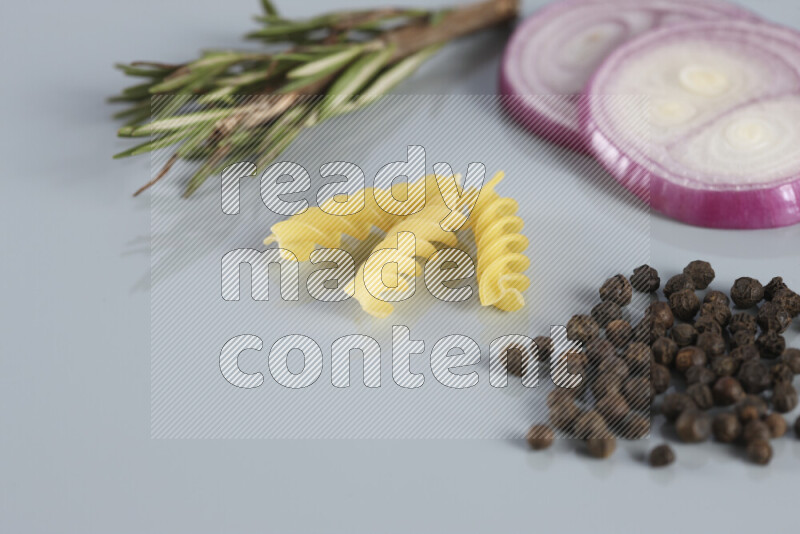 Raw pasta with different ingredients such as cherry tomatoes, garlic, onions, red chilis, black pepper, white pepper, bay laurel leaves, rosemary, cardamom and mushrooms on light blue background