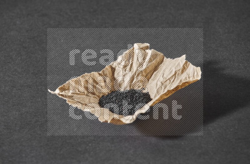 A crumpled piece of paper full of black seeds on a black flooring