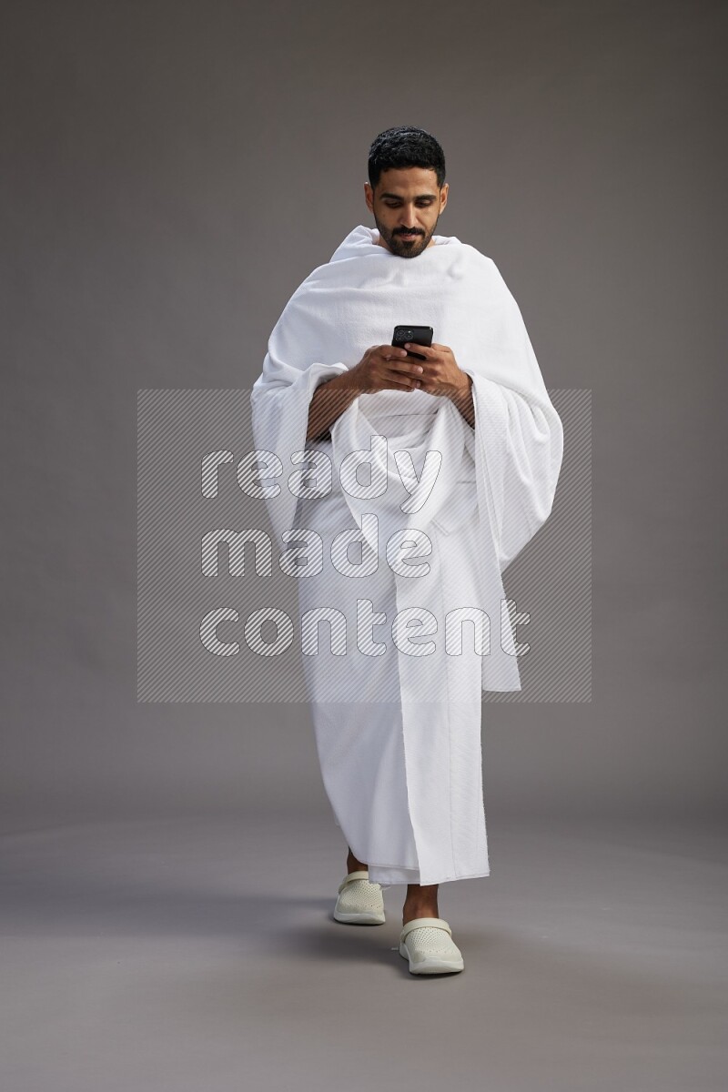 A man wearing Ehram Standing texting on phone on gray background