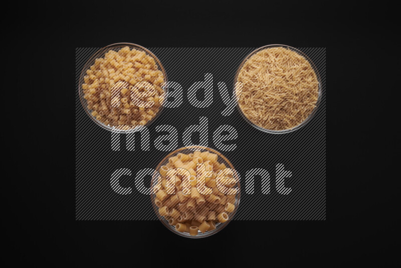 Different pasta types in glass bowls on black background