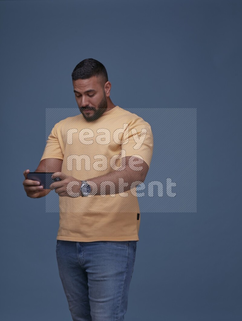 A man Playing Games on Smartphone on Blue Background wearing Orange T-shirt