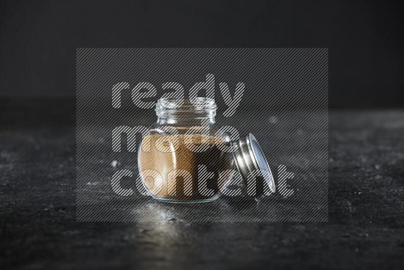 وعاء زجاجي للتوابل ممتلئ ببودرة الكمون على خلفية سوداء