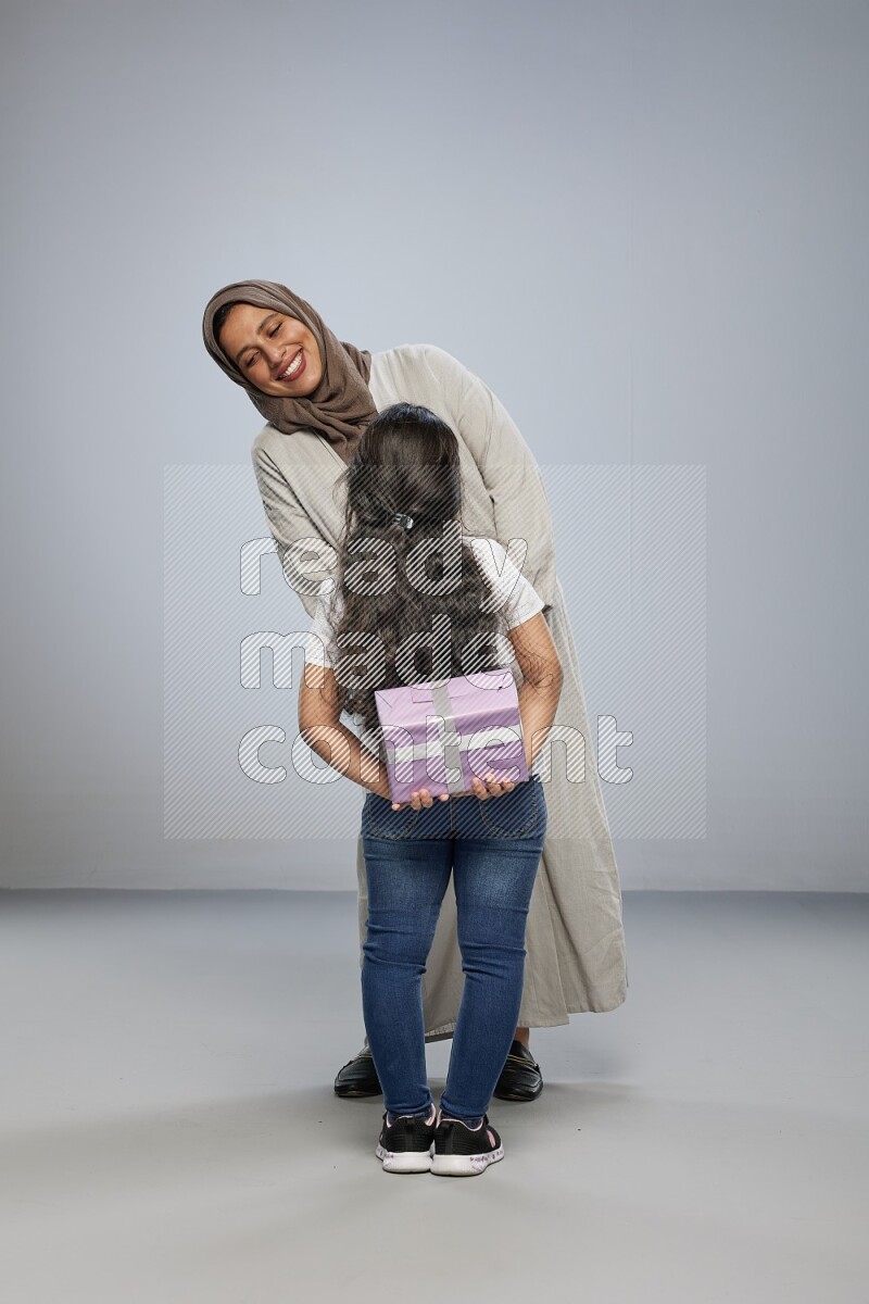 A girl standing hiding a gift behind her back for her mother on gray background