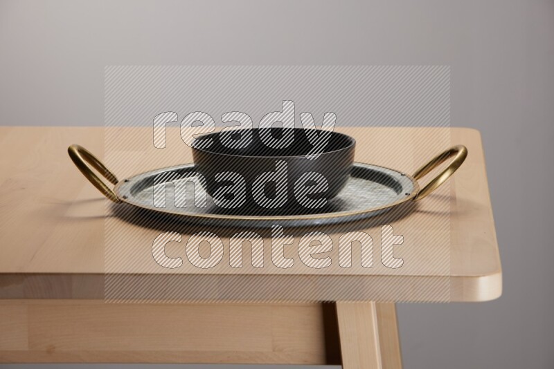 black bowl placed on a rounded stainless steel tray with golden handels on the edge of wooden table