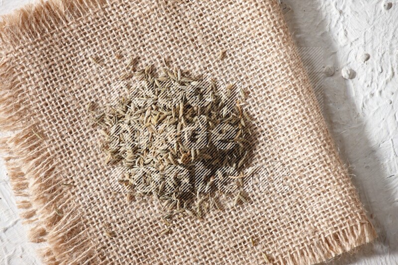 Cumin seeds on a burlap piece on a textured white flooring