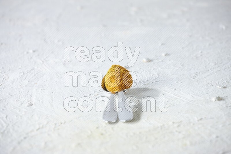 ملعقتان معدنيتان مليئتان ببودرة الكركم علي خلفية بيضاء