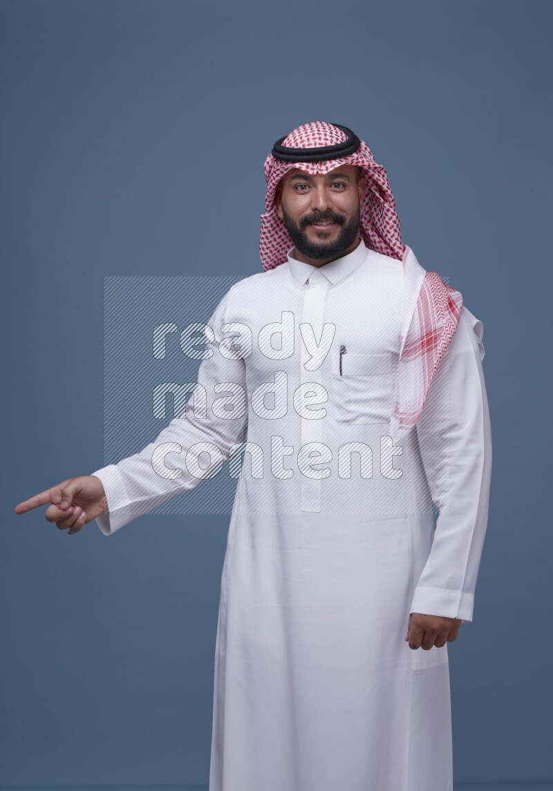 A man pointing on blue background wearing Saudi Thob with Shomag