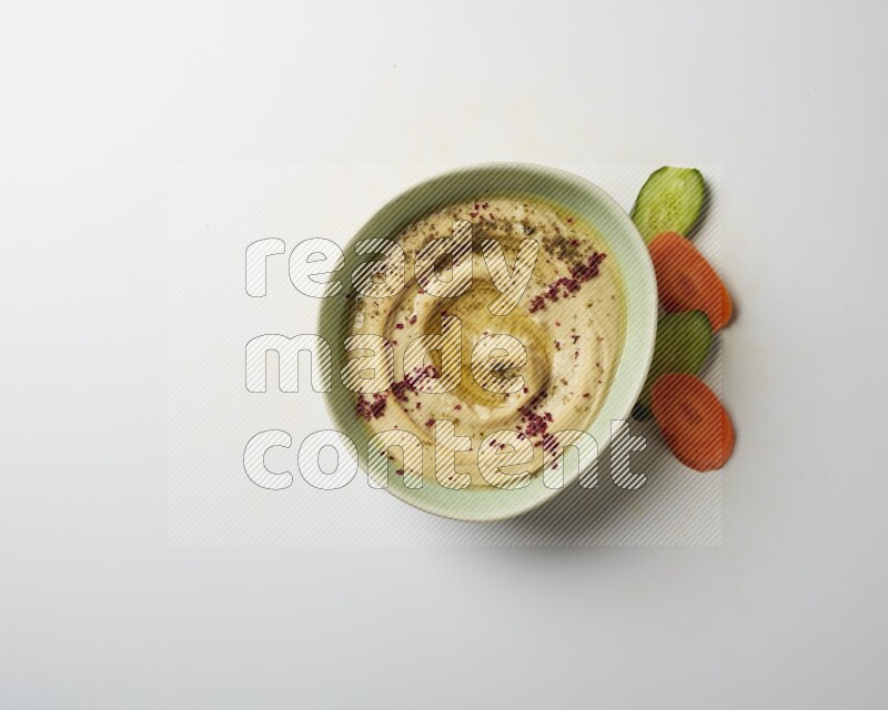Hummus in a green plate garnished with zattar & sumak on a white background