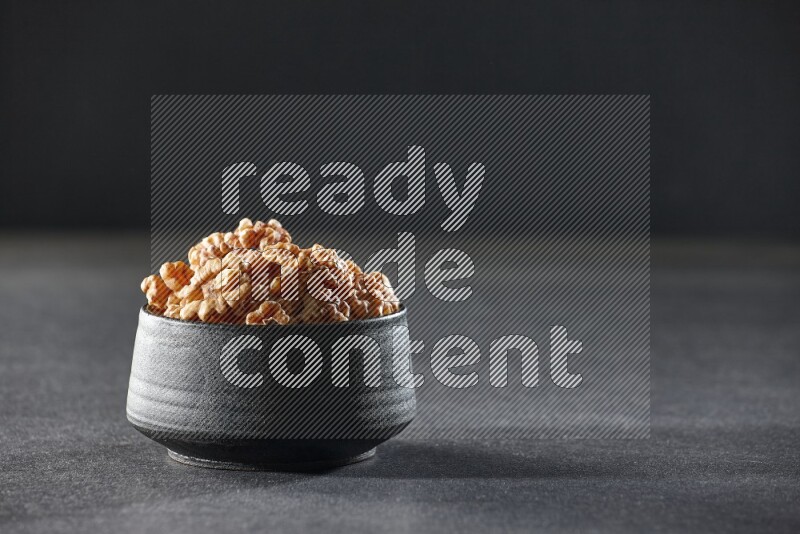 A black pottery bowl full of peeled walnuts on a black background in different angles