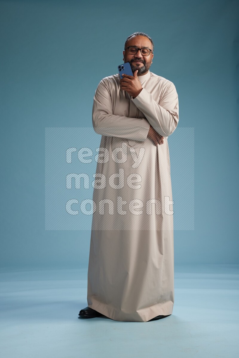 Saudi Man without shimag Standing texting on phone on blue background