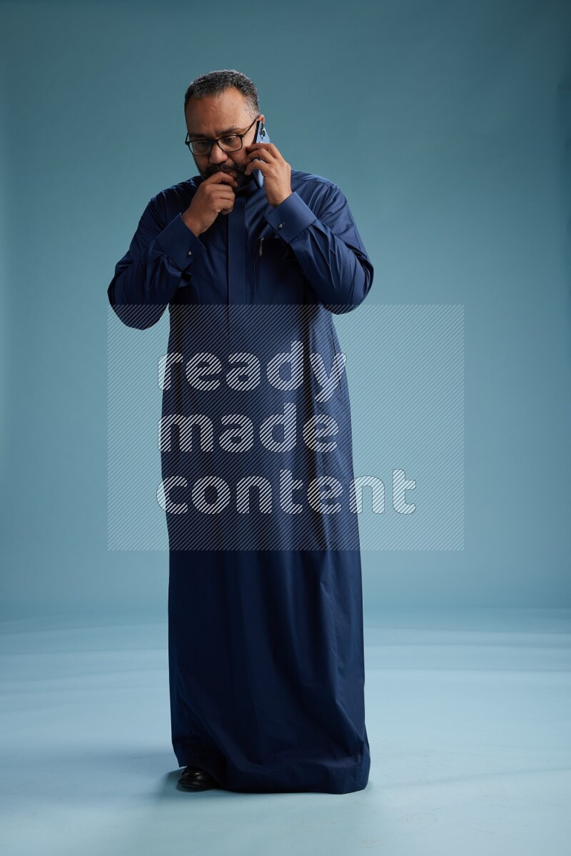 Saudi Man without shimag Standing talking on phone on blue background