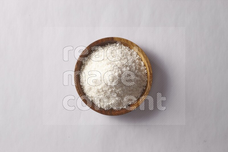 Desiccated coconuts in a wooden bowl on white background