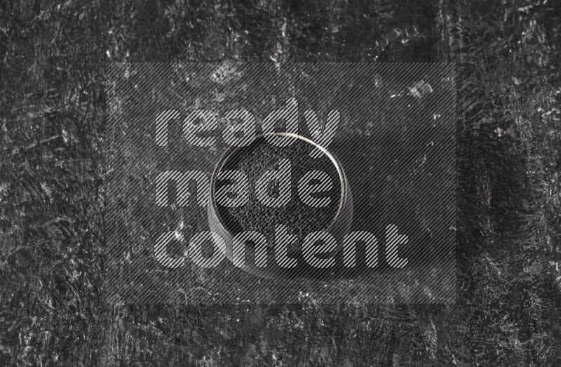 A black pottery bowl full of black seeds on a textured black flooring