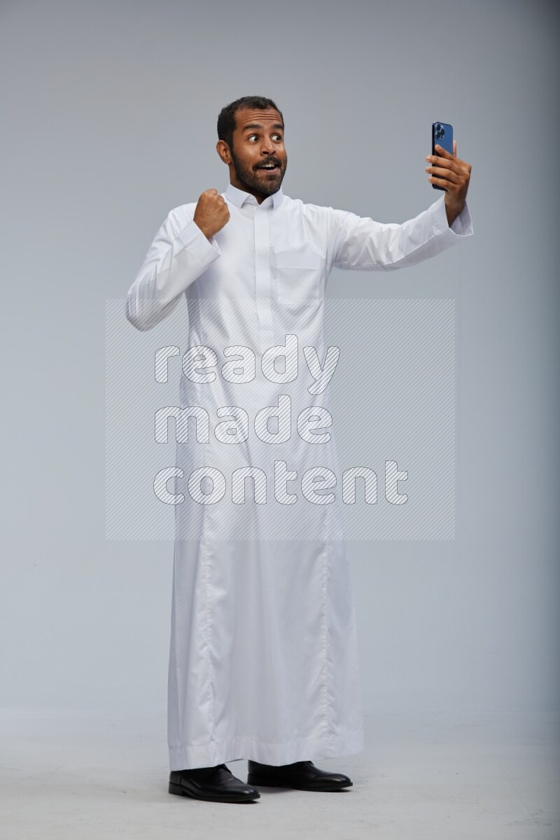 Saudi man wearing Thob standing taking selfie on Gray background