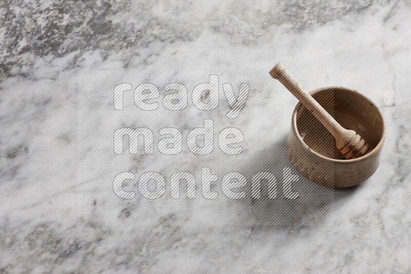 Multicolored pottery bowl with wooden honey dipper in it on grey marble background