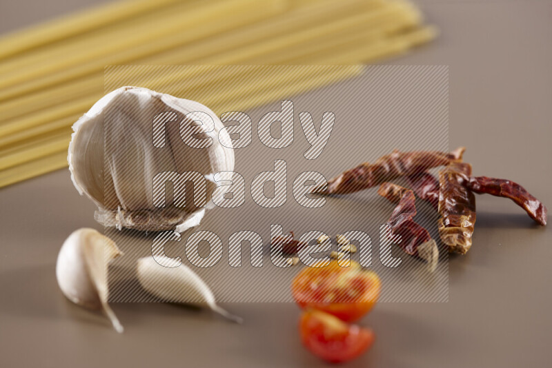 Raw pasta with different ingredients such as cherry tomatoes, garlic, onions, red chilis, black pepper, white pepper, bay laurel leaves, rosemary and cardamom on beige background