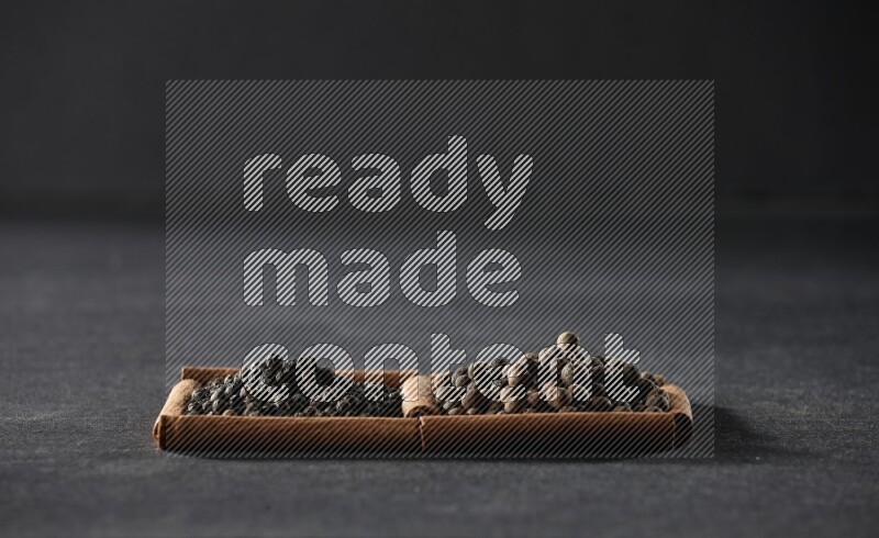 2 squares of cinnamon sticks full of black peppers and allspice on black flooring