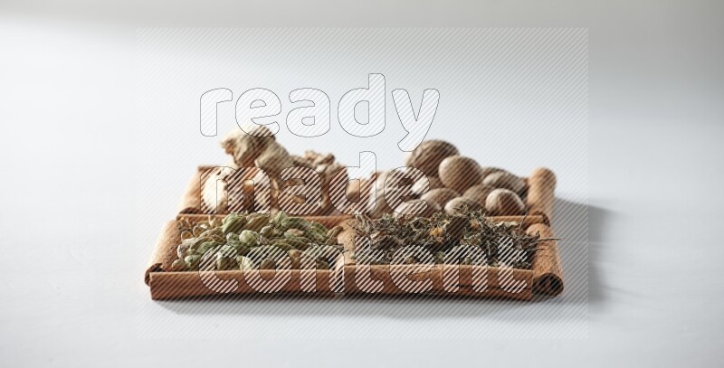 4 مربعات من أعواد القرفة ممتلئة بجوزة الطيب والزنجبيل المجفف والهيل والريحان المجفف على أرضية بيضاء