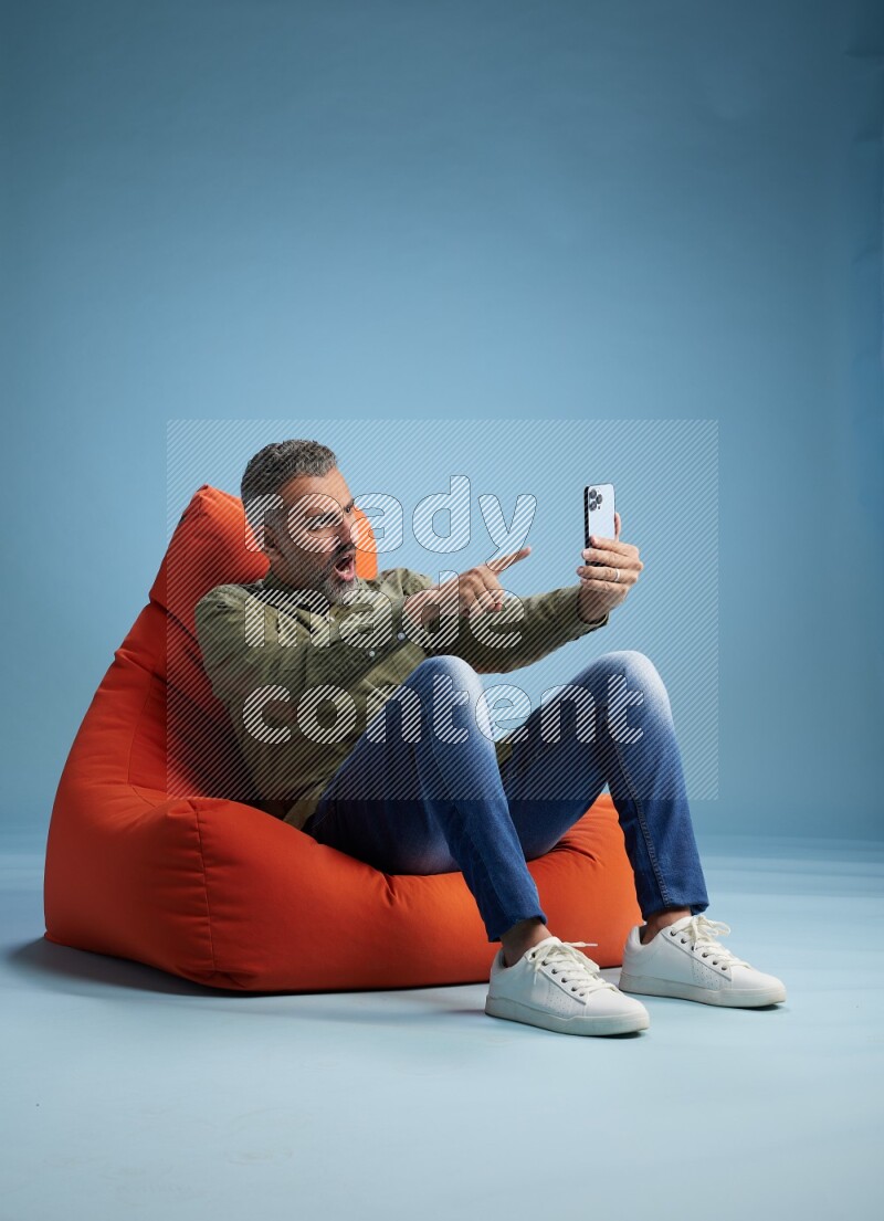 A man sitting on an orange beanbag and taking selfie