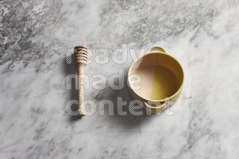 Multicolored pottery bowl with wooden honey dipper on the side on grey marble background