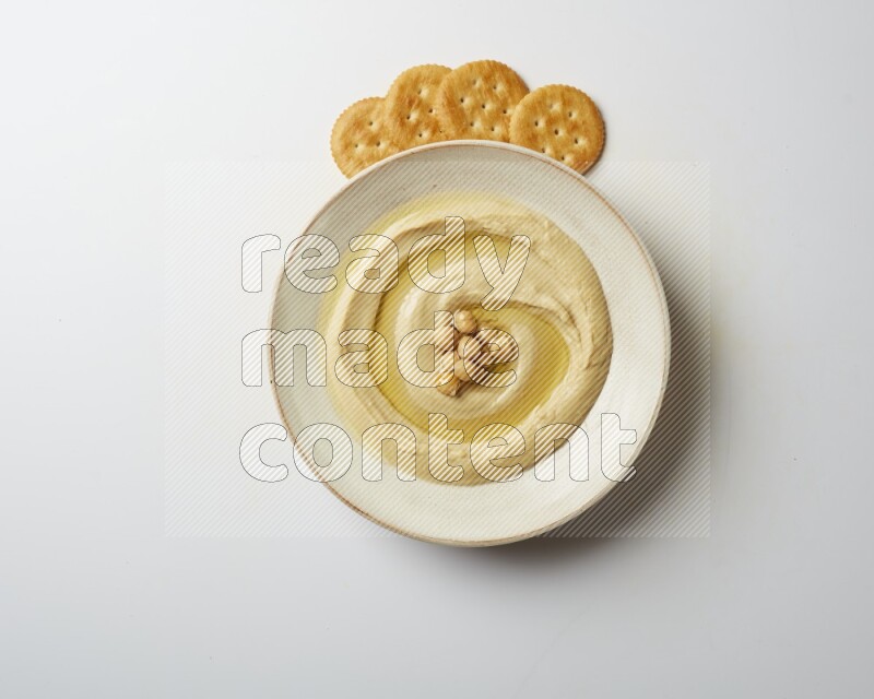 Hummus in a pottry plate garnished with roasted chickpeas on a white background