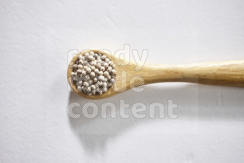 A wooden spoon full of white pepper beads on white flooring