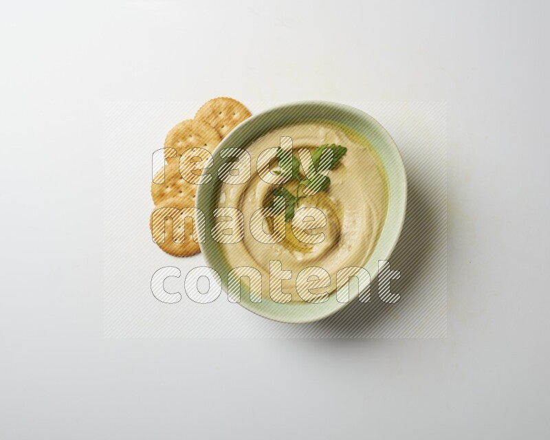 Hummus in a green plate garnished with parsley on a white background