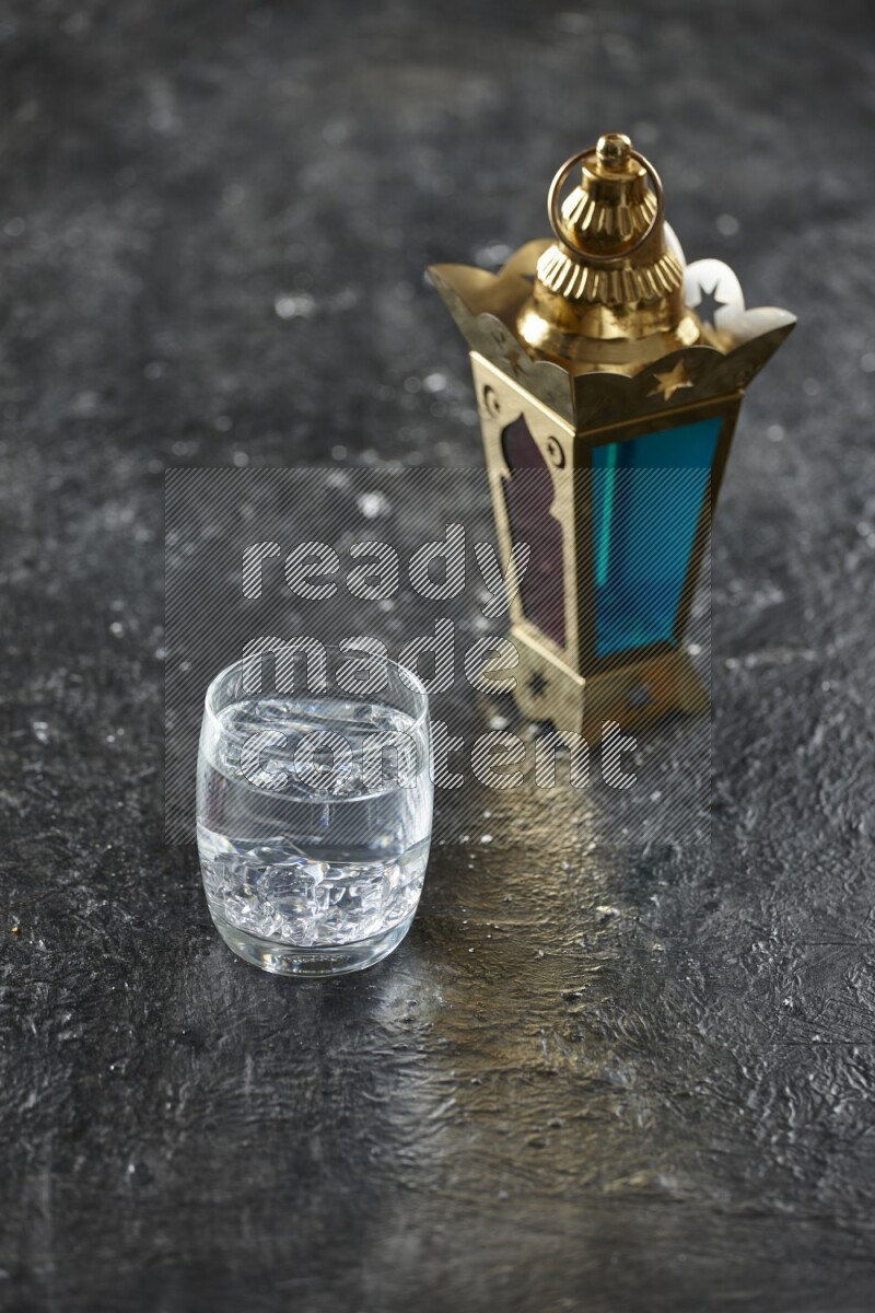 A golden lantern with different drinks, dates, nuts, prayer beads and quran on textured black background