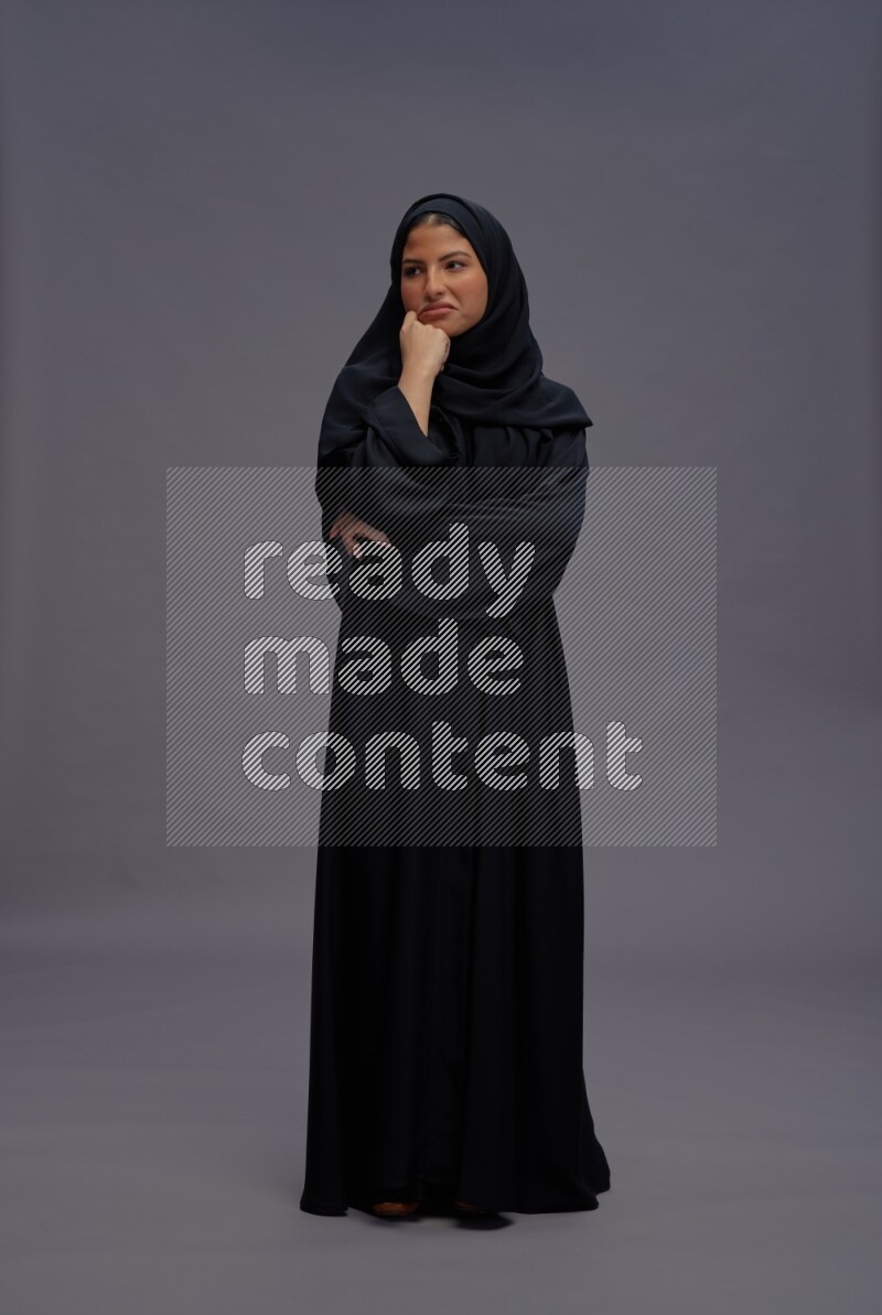 Saudi woman wearing Abaya standing interacting with the camera on gray background