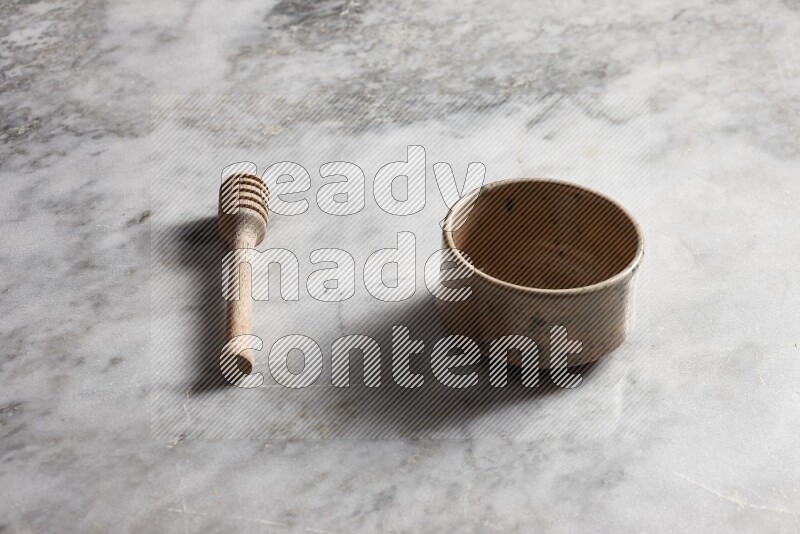 Multicolored pottery bowl with wooden honey dipper on the side on grey marble background