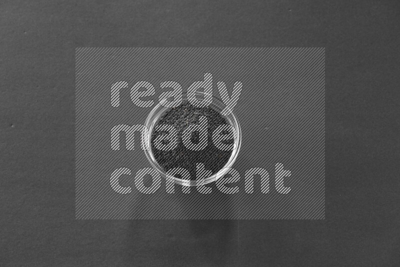 A glass bowl full of black seeds on black flooring