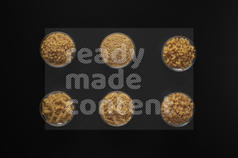 Different pasta types in 6 glass bowls on black background