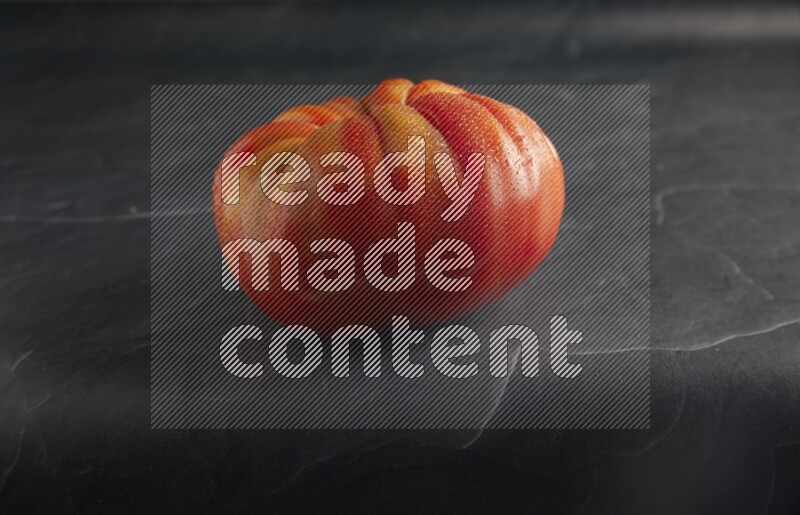 45 degree single heirloom tomato on a textured black slate background