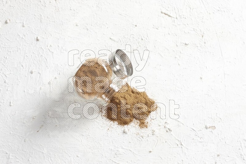 Flipped glass jar full of cinnamon powder on a textured white background